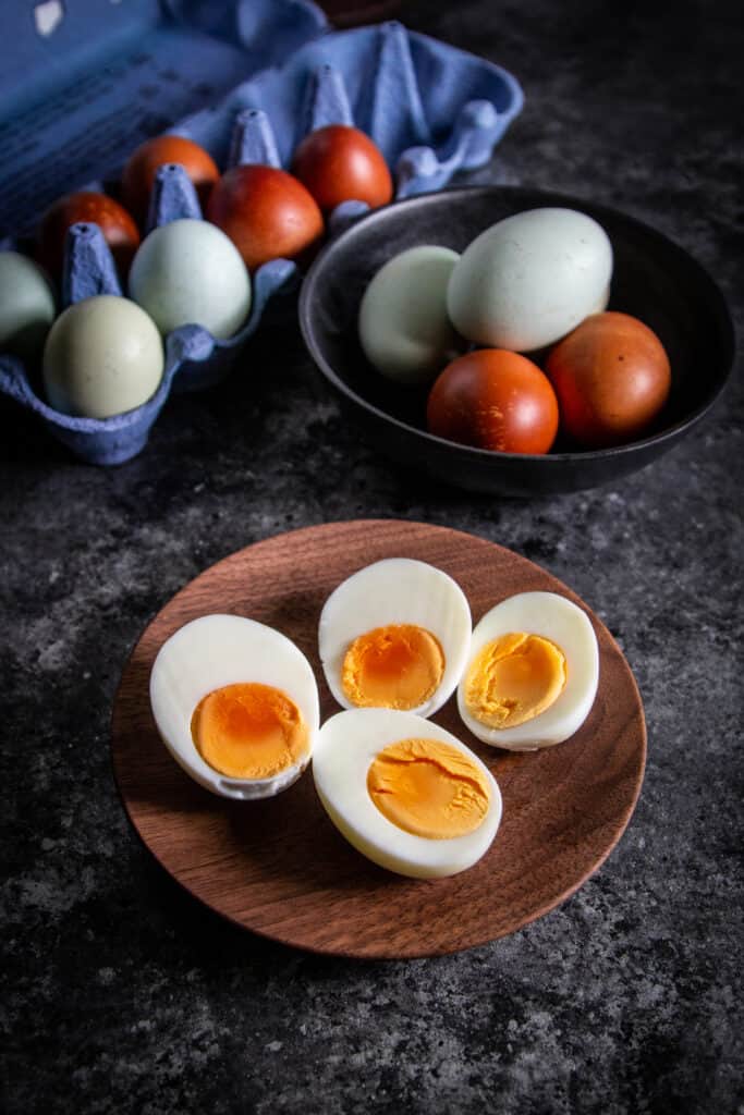 hard-boiled eggs on a wooden plate next to a carton of eggs
