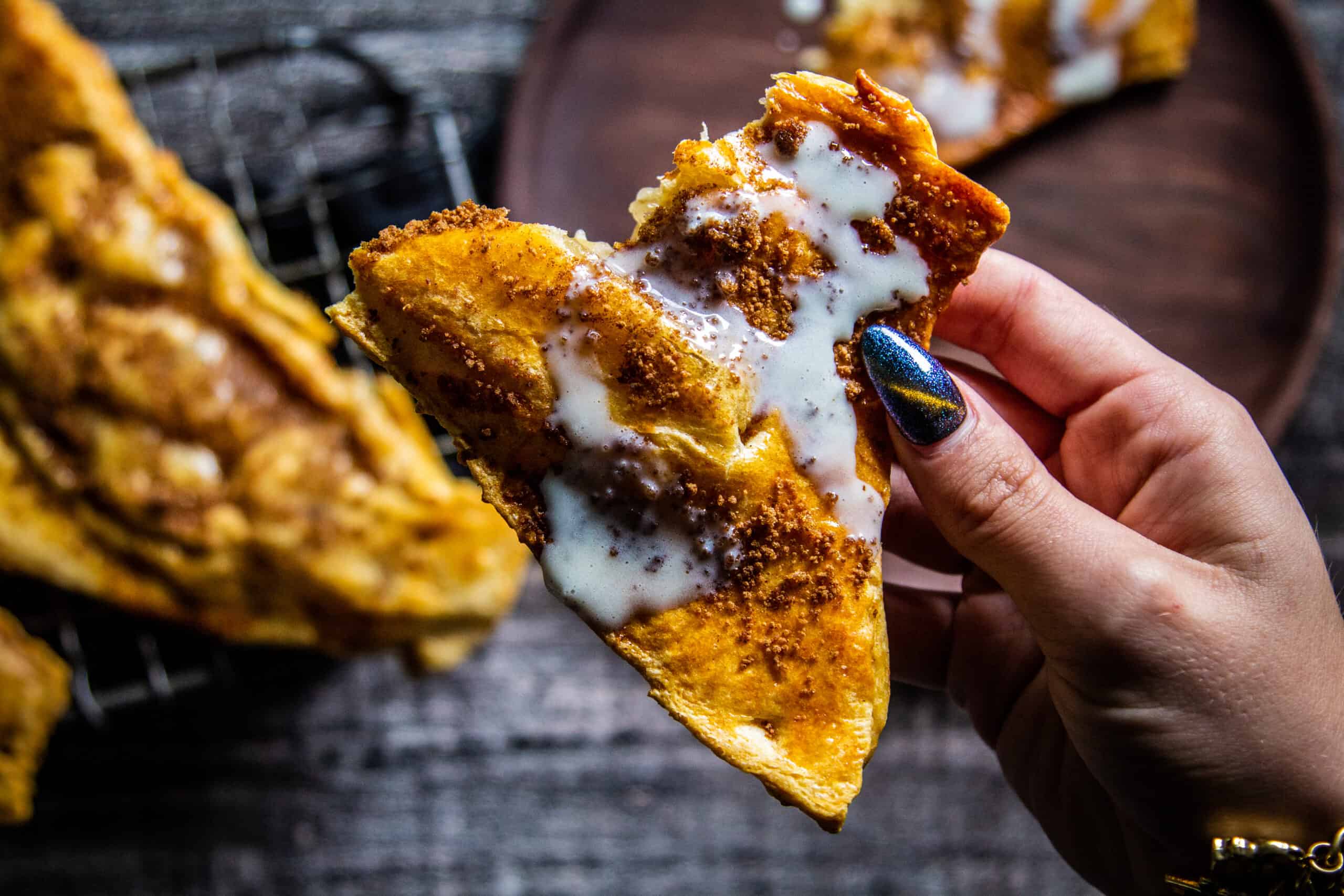 Hand holding a hand pie with icing drizzled over it