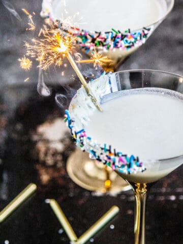 Two martini glasses rimmed with colorful sprinkles & a sparkler