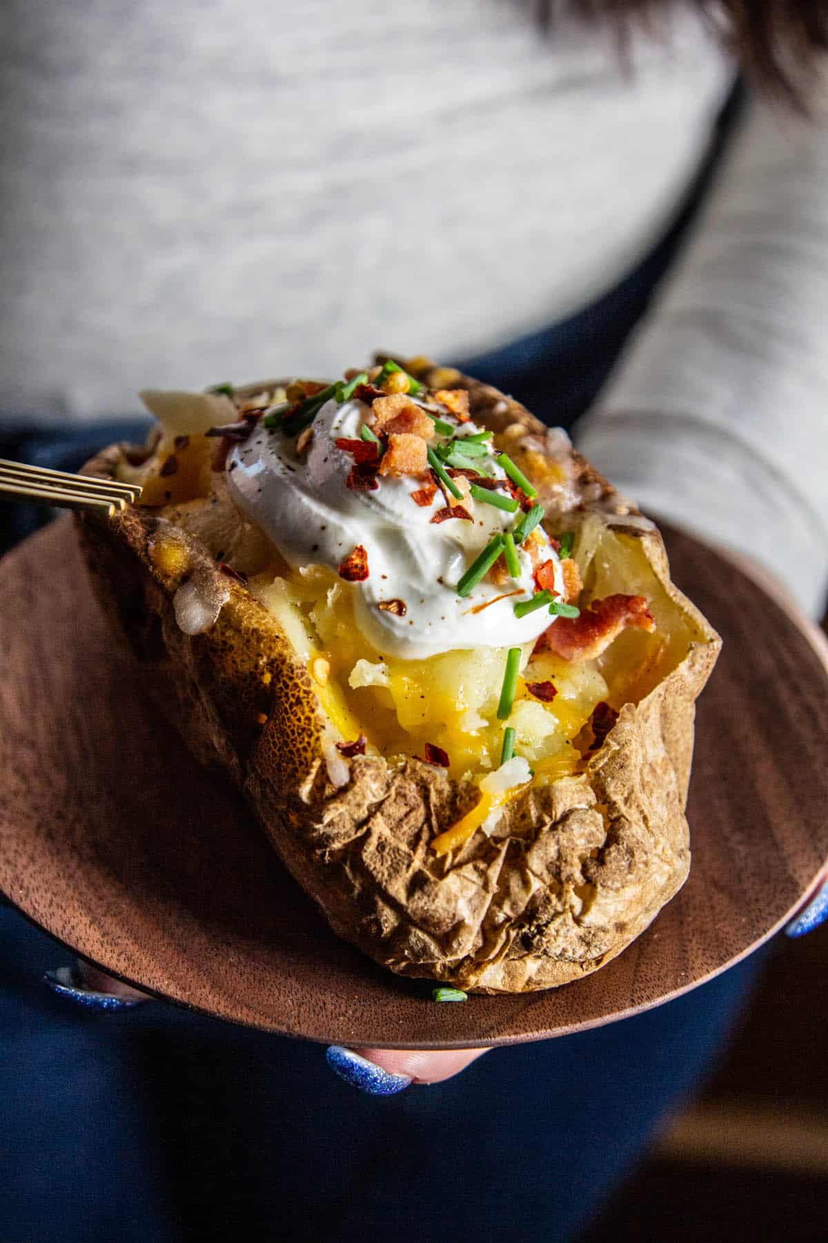 hand holding baked potato with toppings on a wood plate