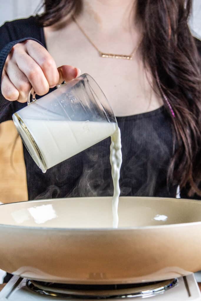 Hand pouring a cup of milk into pan