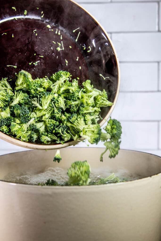 Broccoli getting added into boiling pot of water with macaroni shells
