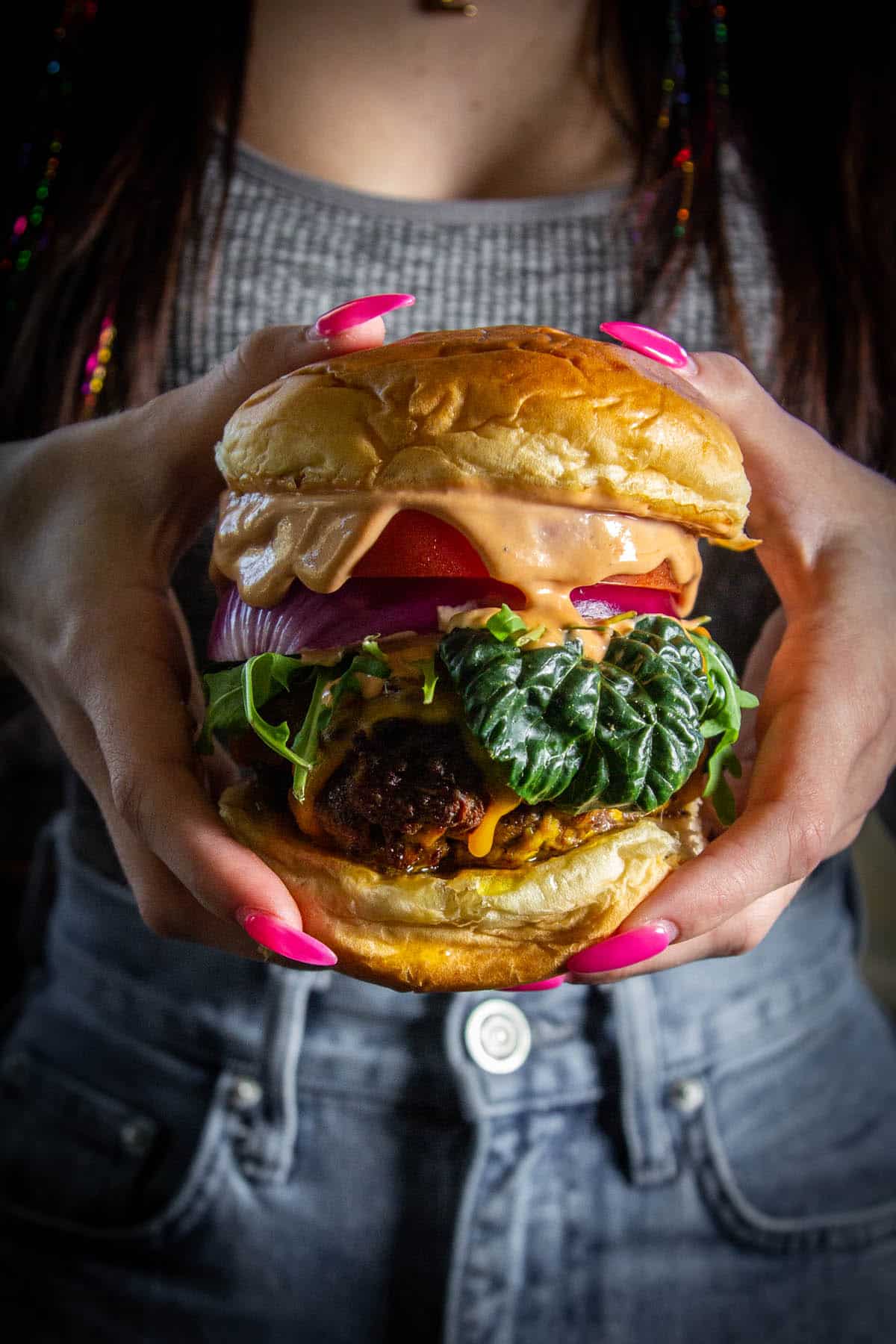 hands with pink nails holding hamburger