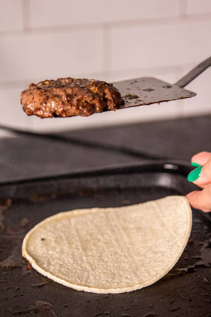 tortilla on griddle with patty on spatula