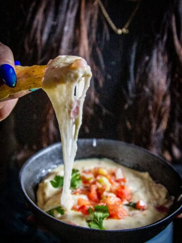 hand holding a chip & scooping queso