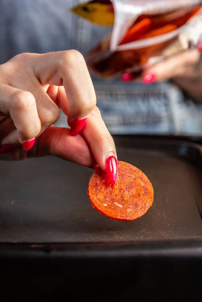 hand placing pepperoni on griddle