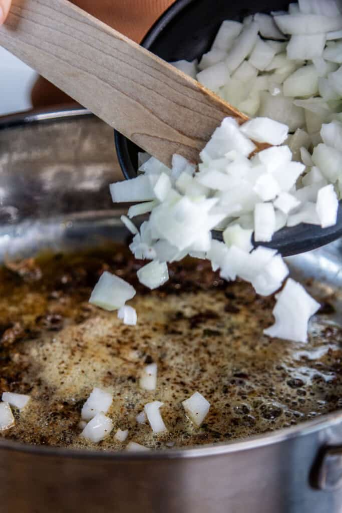 adding raw onions into a pan with butter & garlic