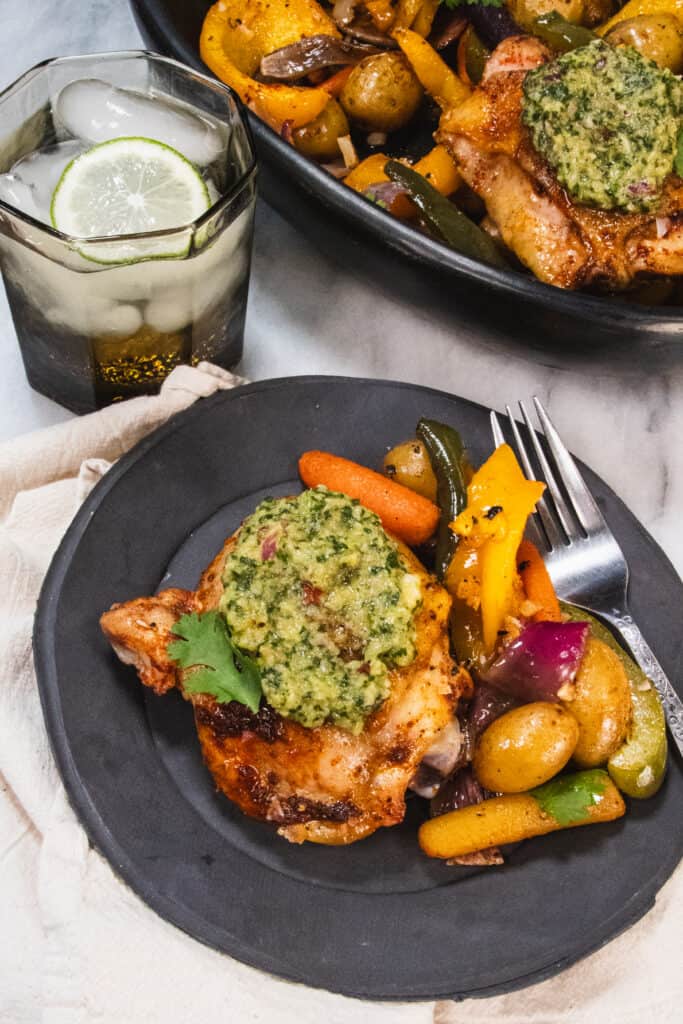 chicken thigh & veggies on a black plate next to water with lime